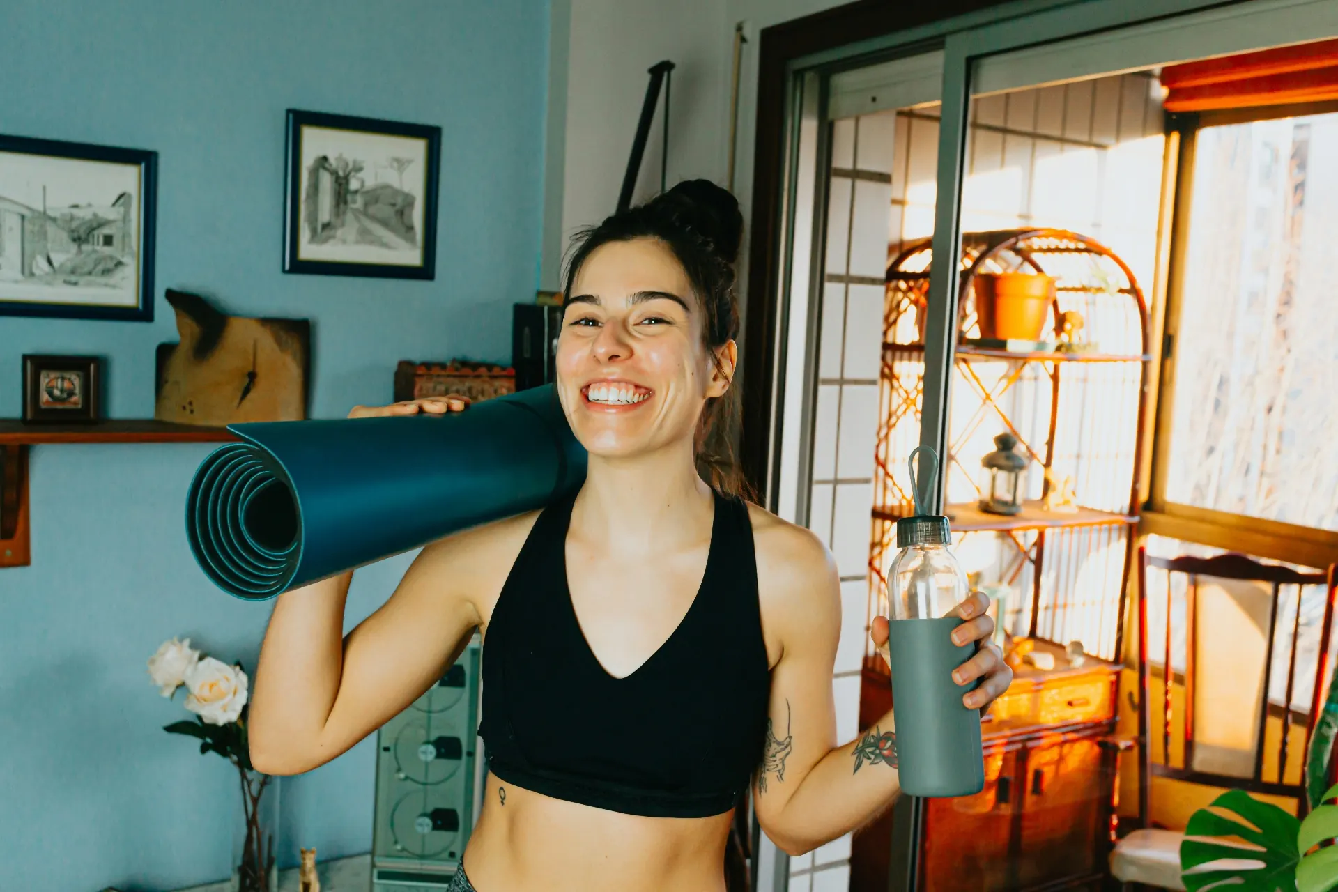 Coach souriante avec tapis de yoga et gourde, sereine chez elle